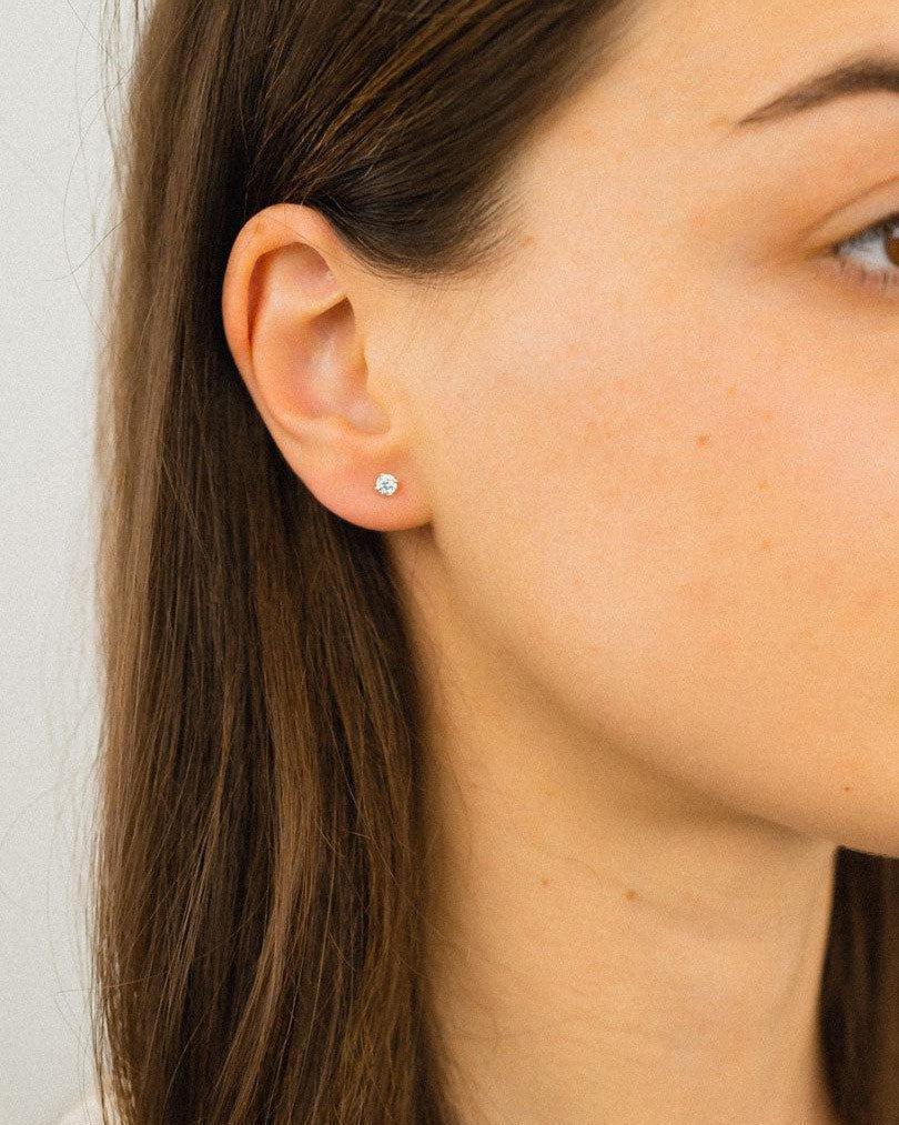 Silver four claw diamond stud earring on an ear.
