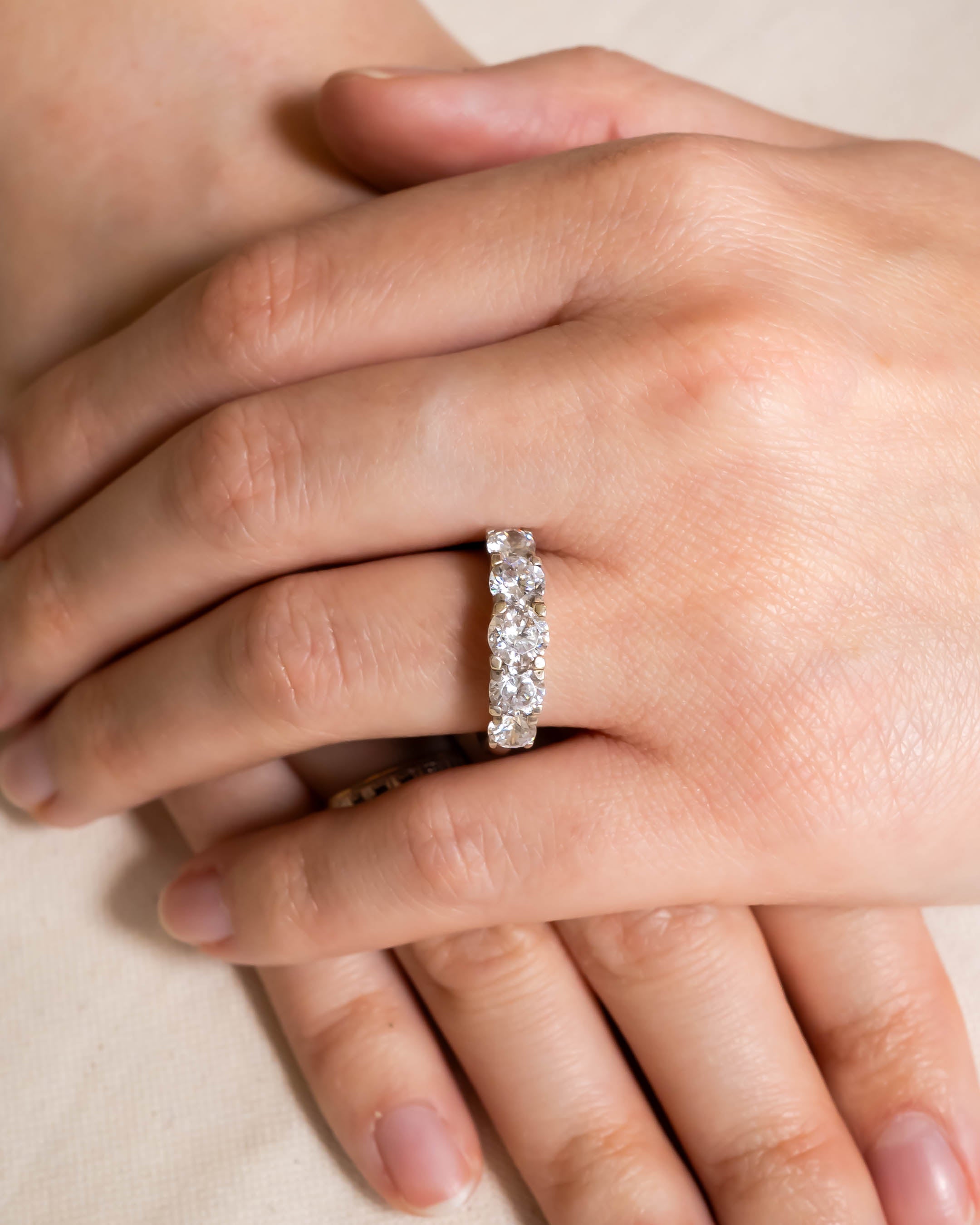 Gold half eternity ring with five oval diamonds in a four-claw setting on a hand.