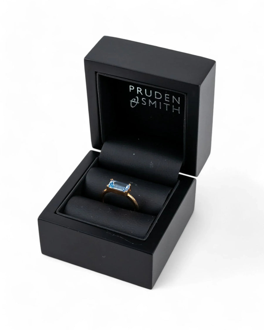 Gold ring with a blue baguette gemstone in a black box.