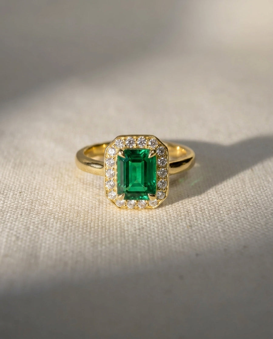 18ct yellow gold engagement ring with an emerald cut emerald surrounded by diamonds.