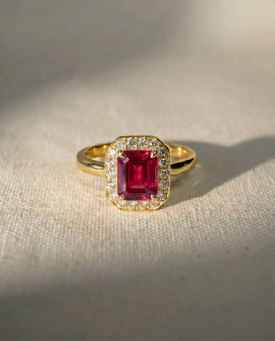 18ct yellow gold engagement ring with an emerald-cut ruby surrounded by diamonds.