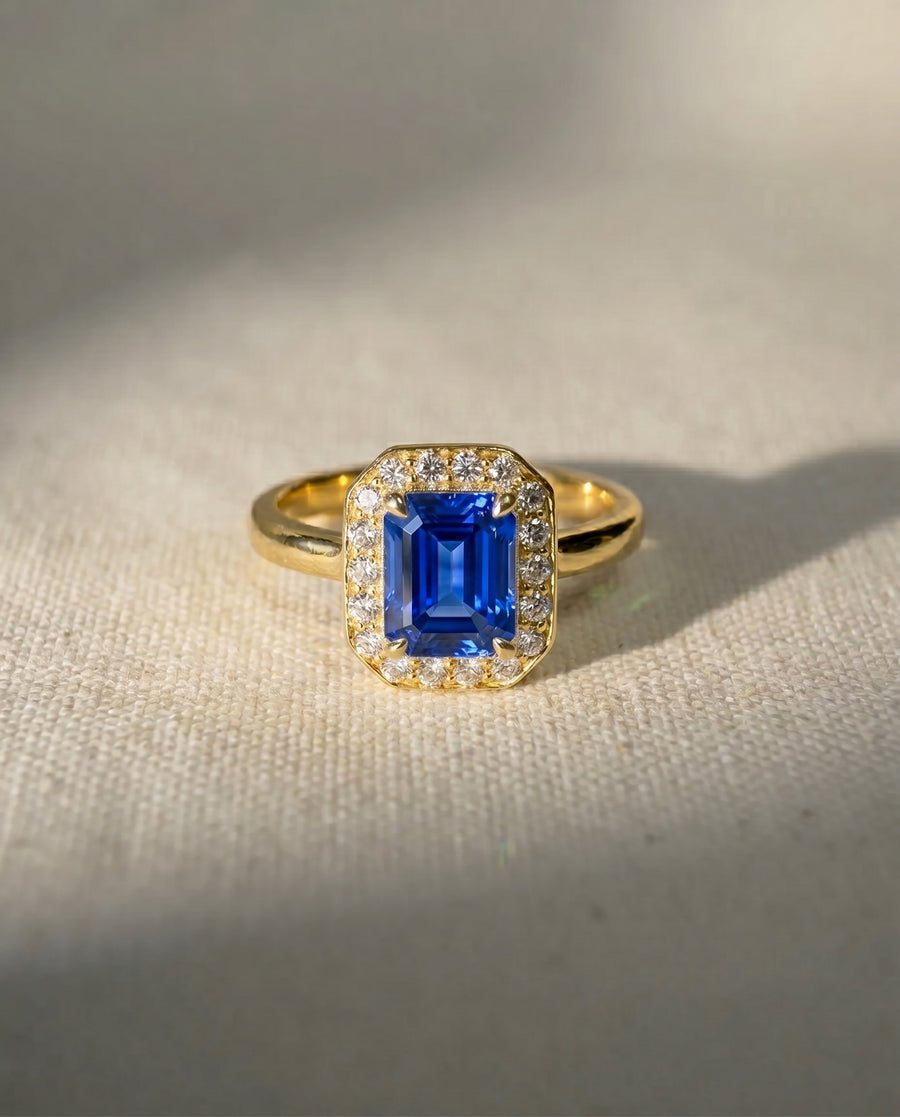 18ct yellow gold engagement ring with an emerald-cut sapphire and diamond cluster.