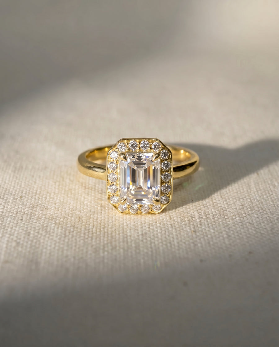 Gold engagement ring with an emerald-cut diamond surrounded by smaller diamonds.