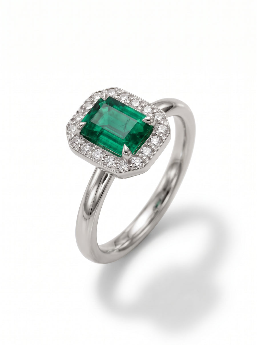 Emerald-cut green emerald engagement ring with a diamond halo set in polished white gold.