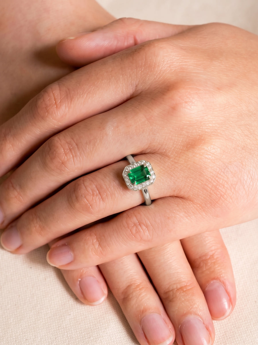 Emerald-cut green gemstone engagement ring with a diamond halo on a silver band worn on a finger.