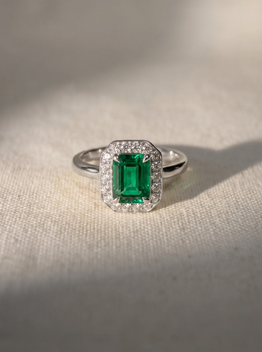 Emerald-cut green gemstone engagement ring with a diamond halo set in a silver-toned metal band.