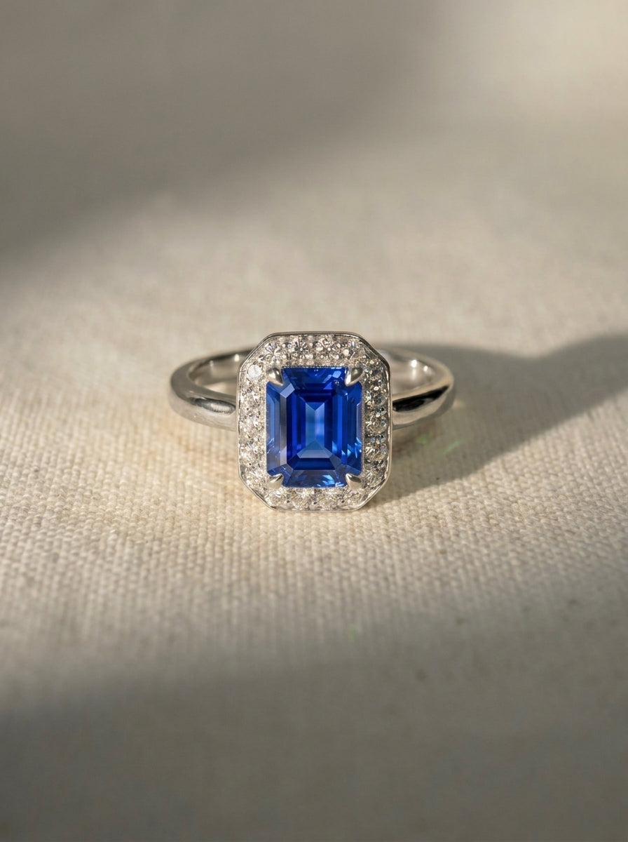 Emerald-cut blue sapphire engagement ring with a diamond halo set in polished white metal.