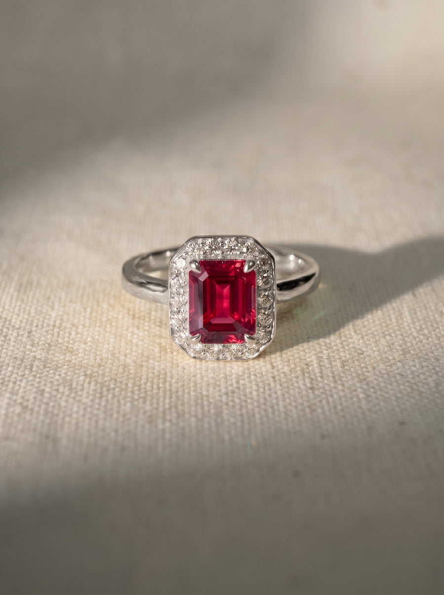 Emerald-cut ruby engagement ring with a diamond halo set in a polished silver-tone metal band.