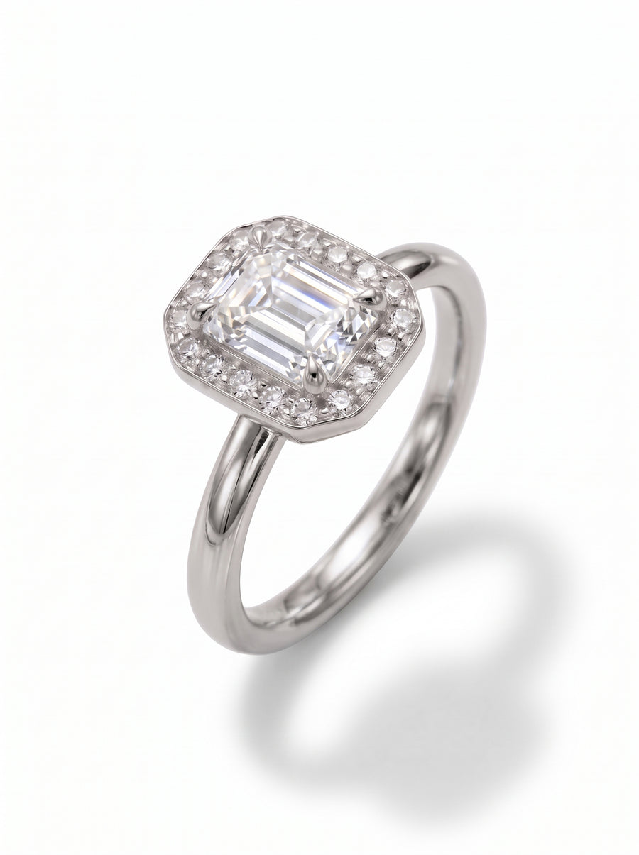 Emerald-cut diamond engagement ring with a halo of small round stones on a polished silver band.