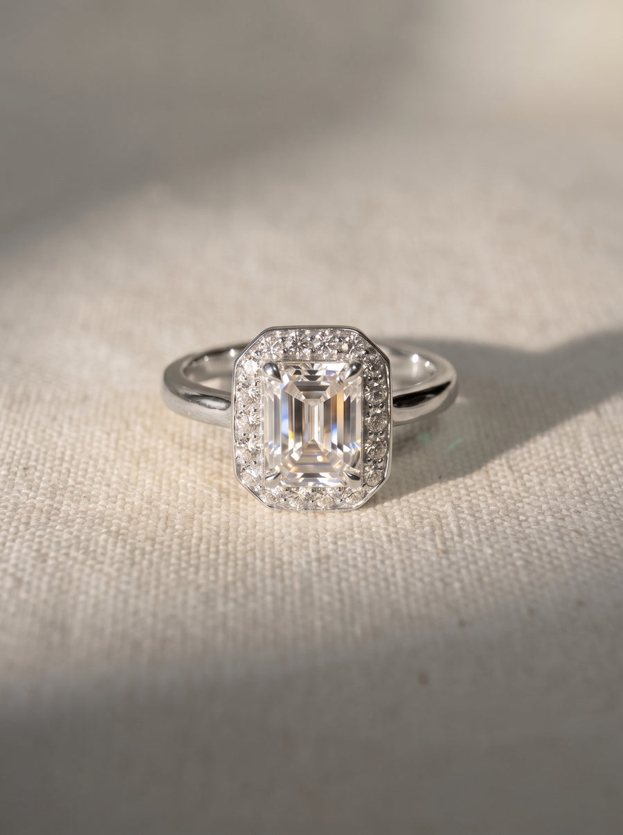 Emerald cut diamond engagement ring with a halo of small diamonds set in polished silver metal.