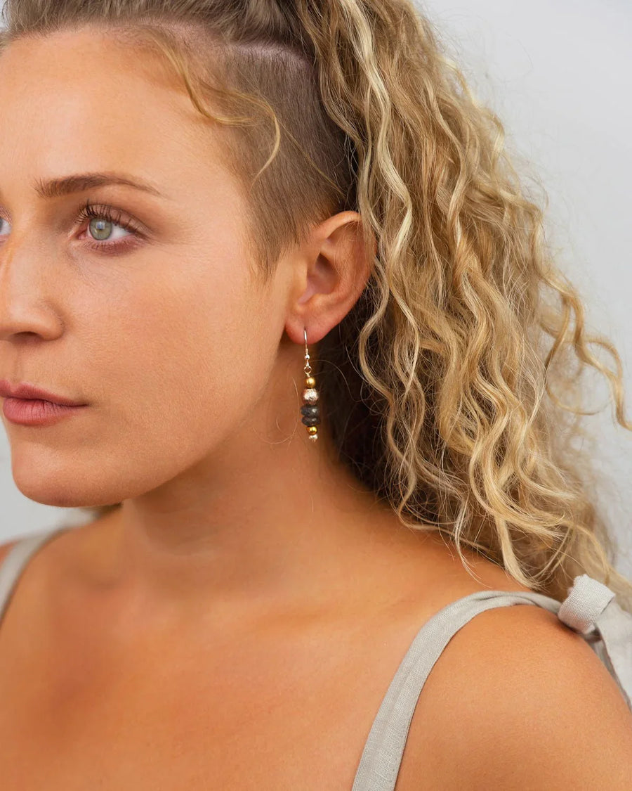 Drop earrings featuring small grey gemstones accented with gold and silver beads worn on a woman's ear.