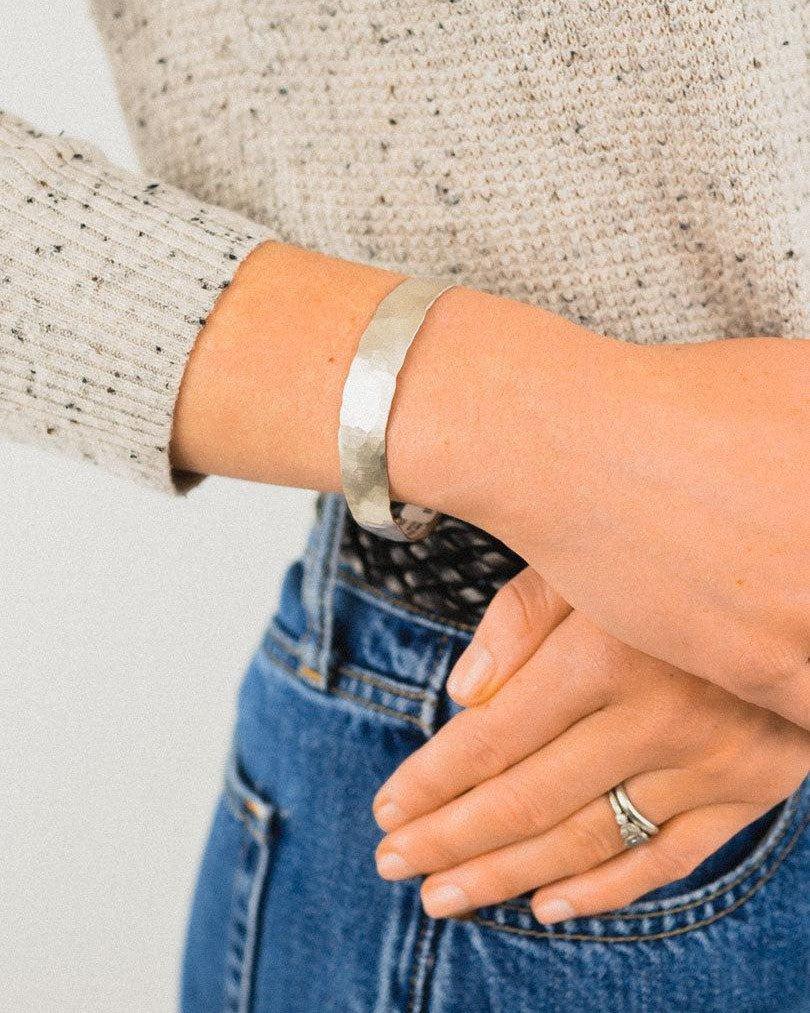 Handcrafted hammered edge matte gold bangle on wrist, casual outfit, artisan jewelry