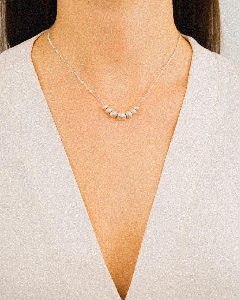 Delicate silver nugget necklace with organic shapes on a fine chain, worn on a woman's neck