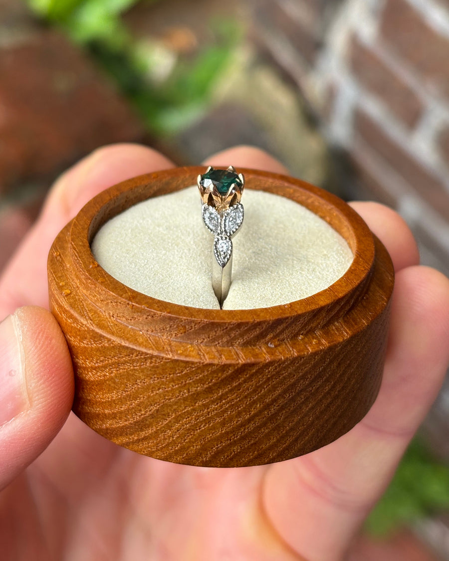 Vintage engagement ring with a green gemstone, rose gold setting, and diamond accents on a silver band.