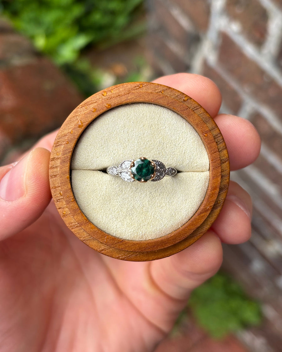 Round green diamond engagement ring in 18ct rose gold and platinum with side accent stones in a wooden box.