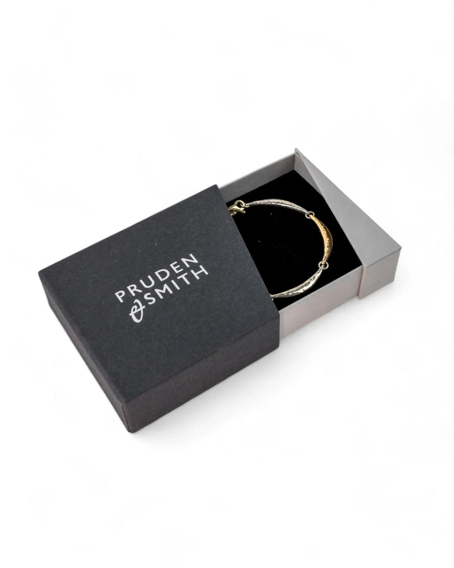 Hammered crescent silver and gold bracelet in a black gift box on white background