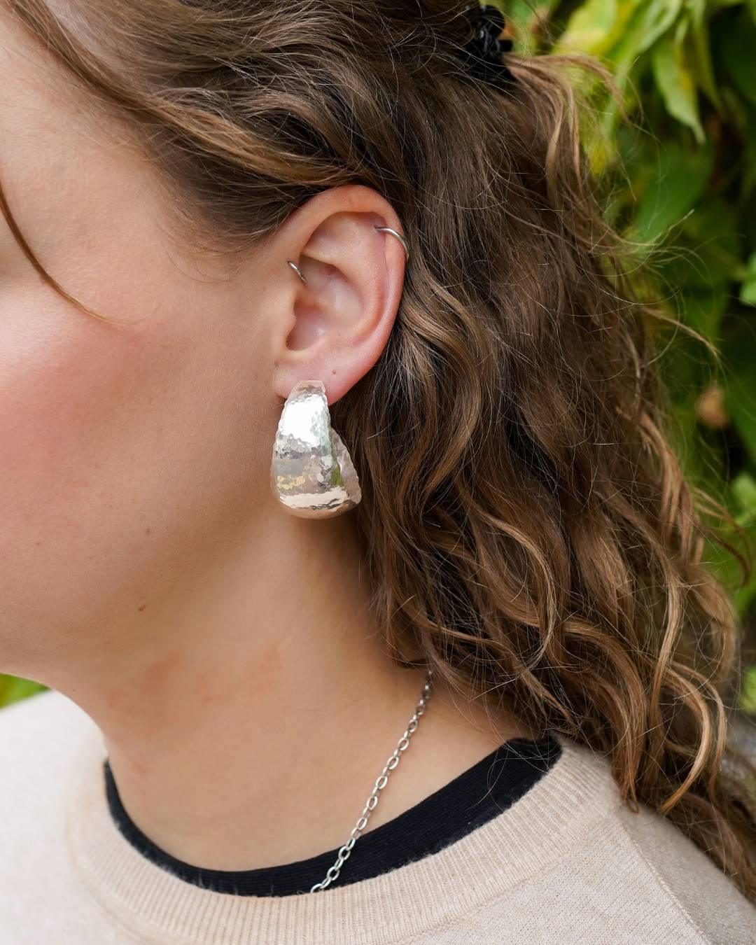 Woman wearing a large hammered silver hoop earring and chain necklace outdoors