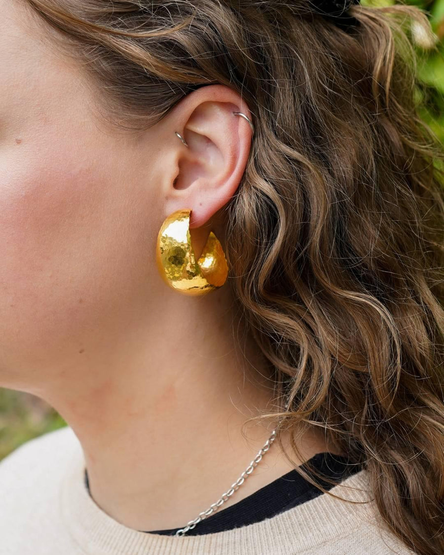 Woman wearing large handmade gold textured hoop earring and a silver chain necklace
