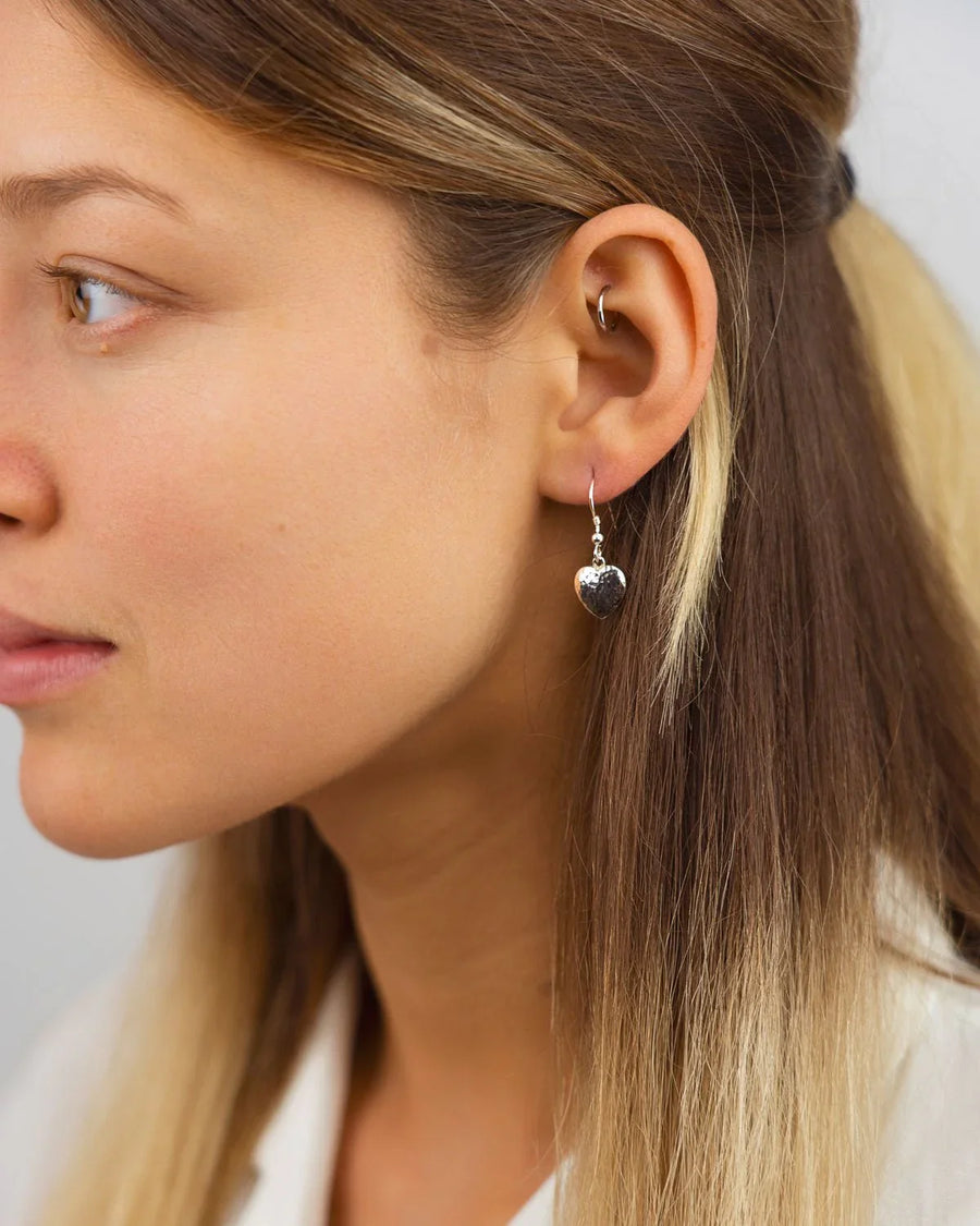 Silver hammered heart drop earrings on a woman's ear.