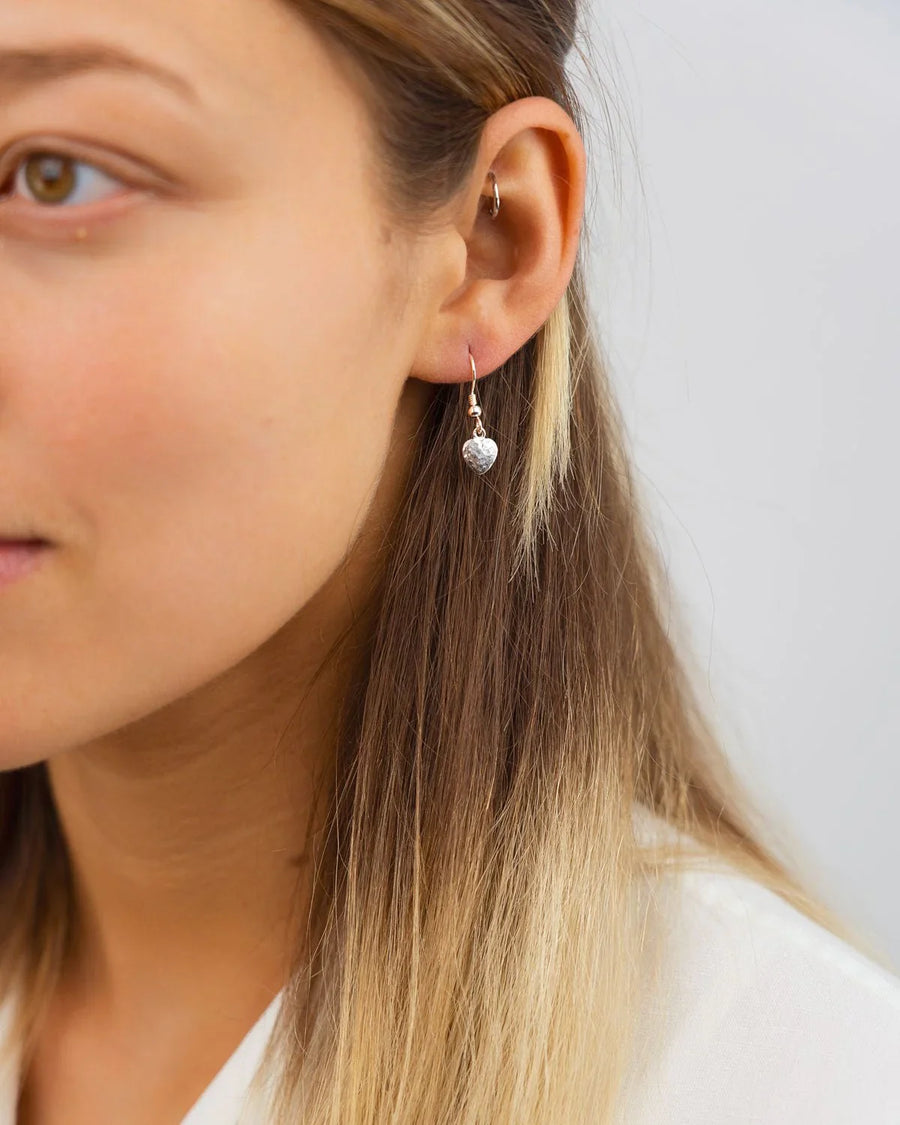 Silver hammered heart drop earring on a woman's ear.