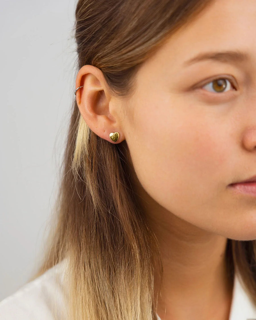 Gold hammered heart stud earring on a woman's ear.