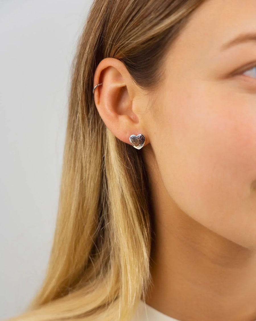 Silver hammered heart stud earring on an ear.