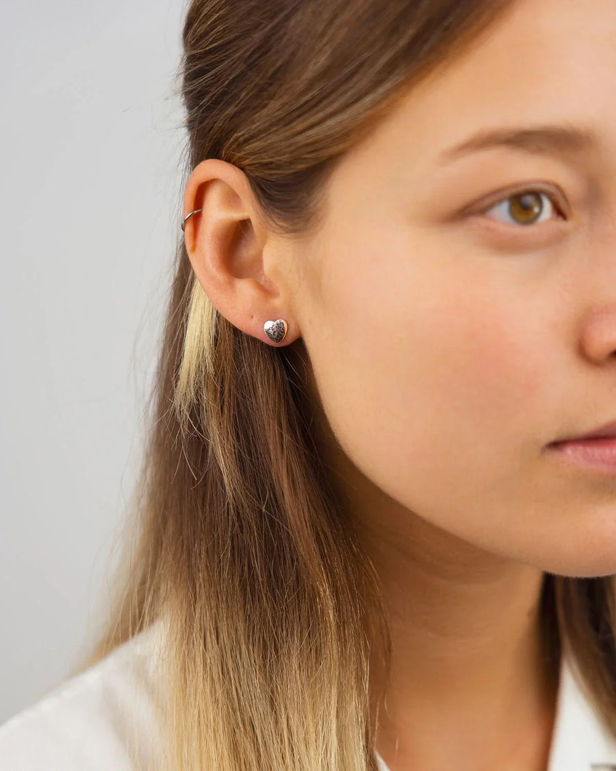 Silver hammered heart stud earrings on a woman's ear.