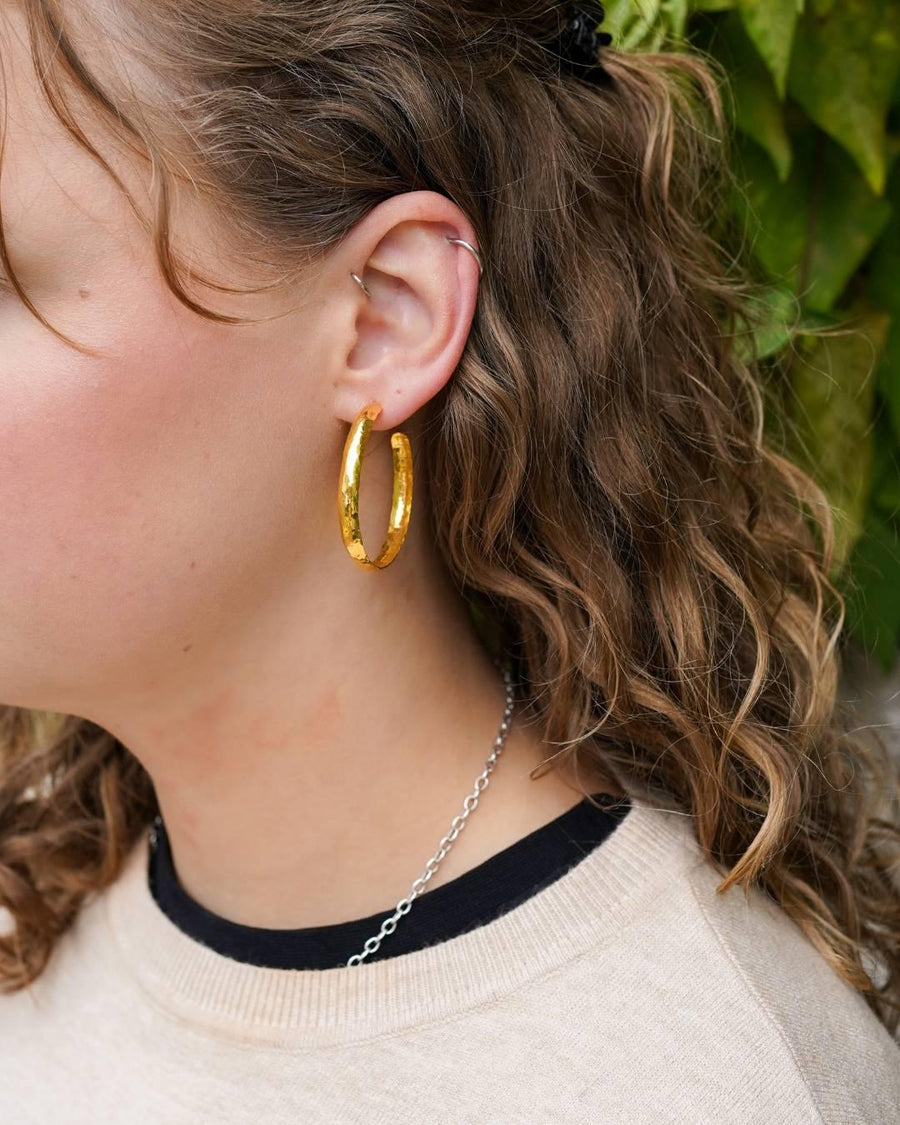 Woman wearing handmade gold hammered hoop earrings and silver chain necklace outdoors