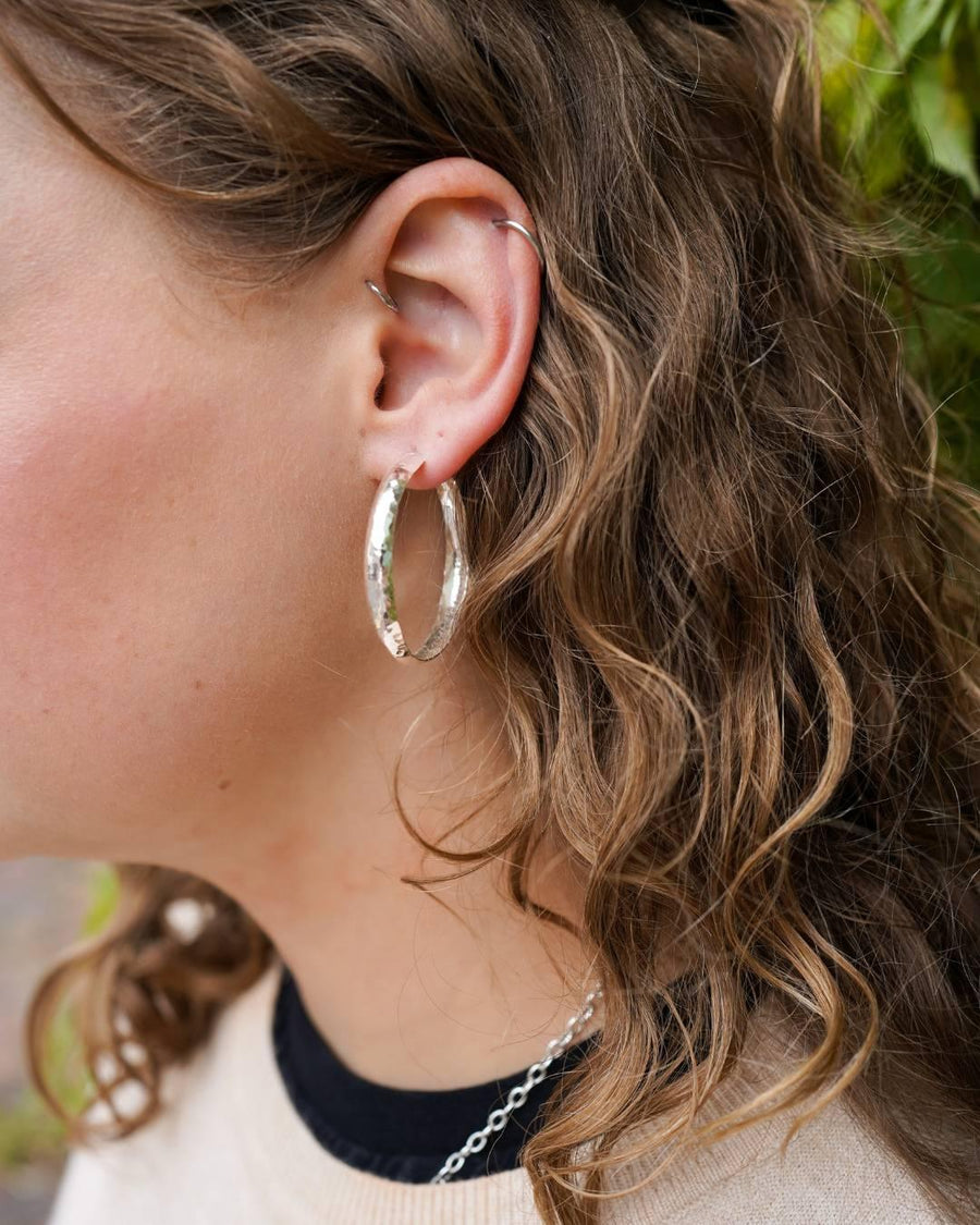 Woman with curly hair wearing handmade hammered silver hoop earrings and ear cuff