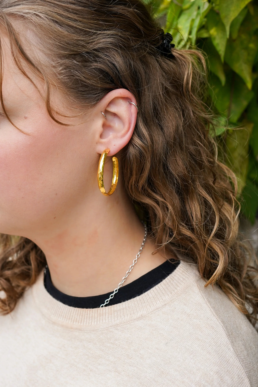 Hammered rough gold hoop earrings on a person's ear.