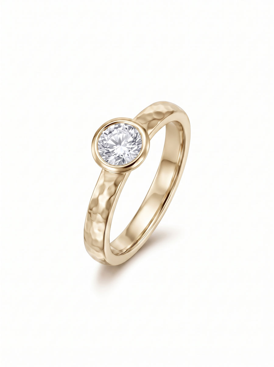 Gold ring with a hammered texture and a round brilliant cut diamond in a bezel setting.
