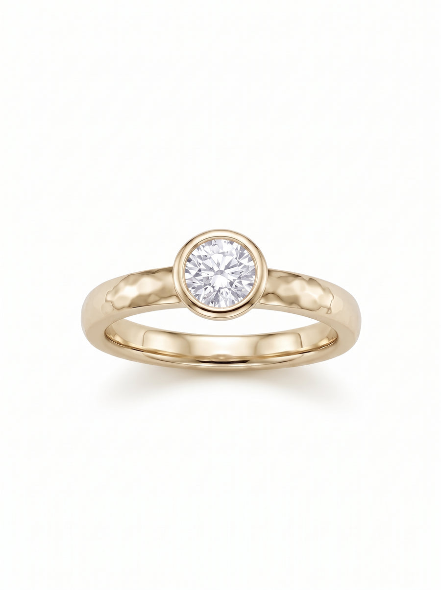 Round brilliant cut diamond set in a hammered yellow gold band with a bezel setting.