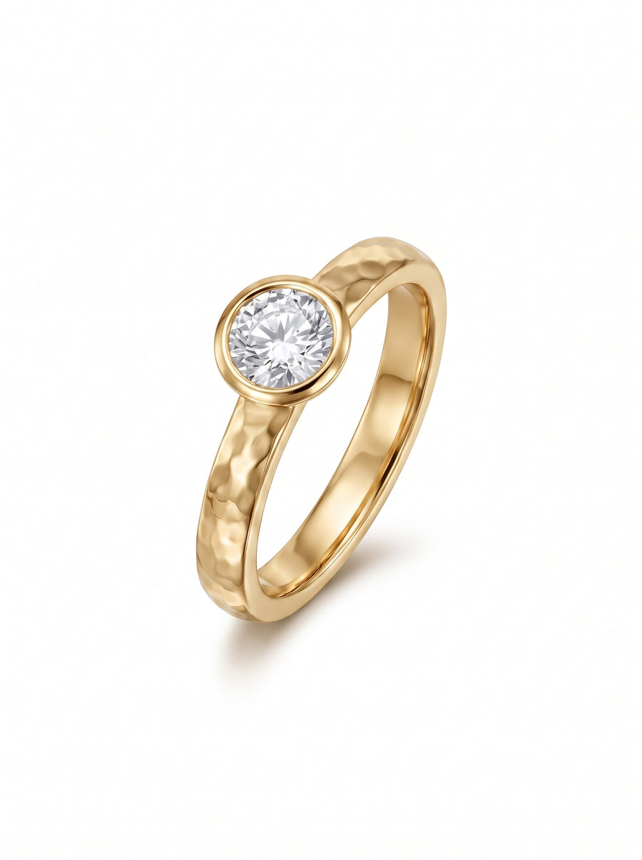 Gold ring with a hammered texture and a round brilliant cut diamond in a bezel setting.