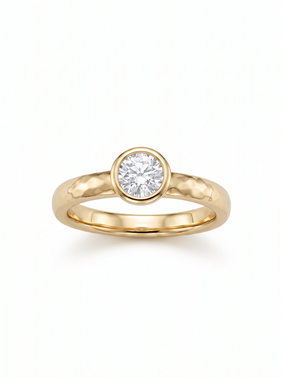 Round brilliant cut diamond set in a hammered yellow gold band with a bezel setting.