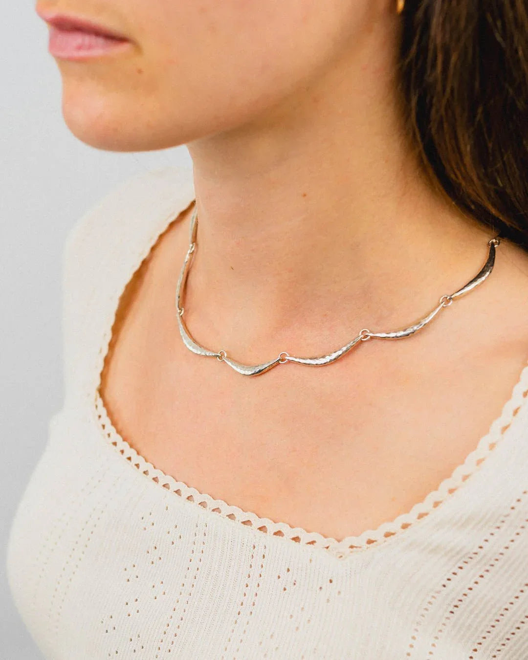 Hammered silver and gold crescent necklace on woman wearing cream knit top
