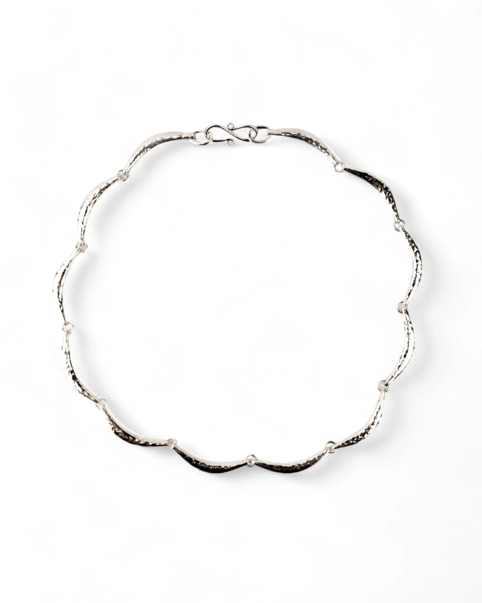 Hammered silver crescent necklace with organic, textured links on a white background