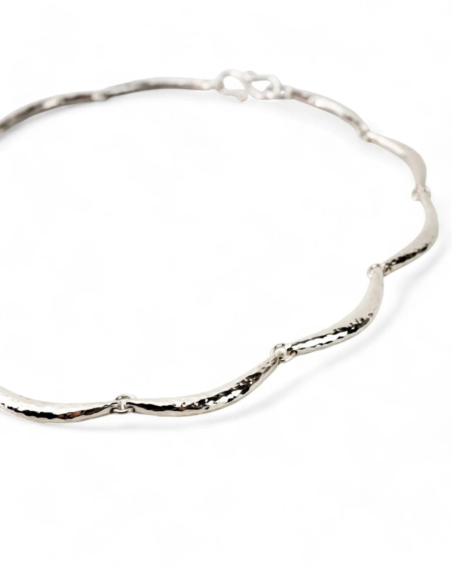 Hammered silver crescent necklace with organic, textured design on a white background
