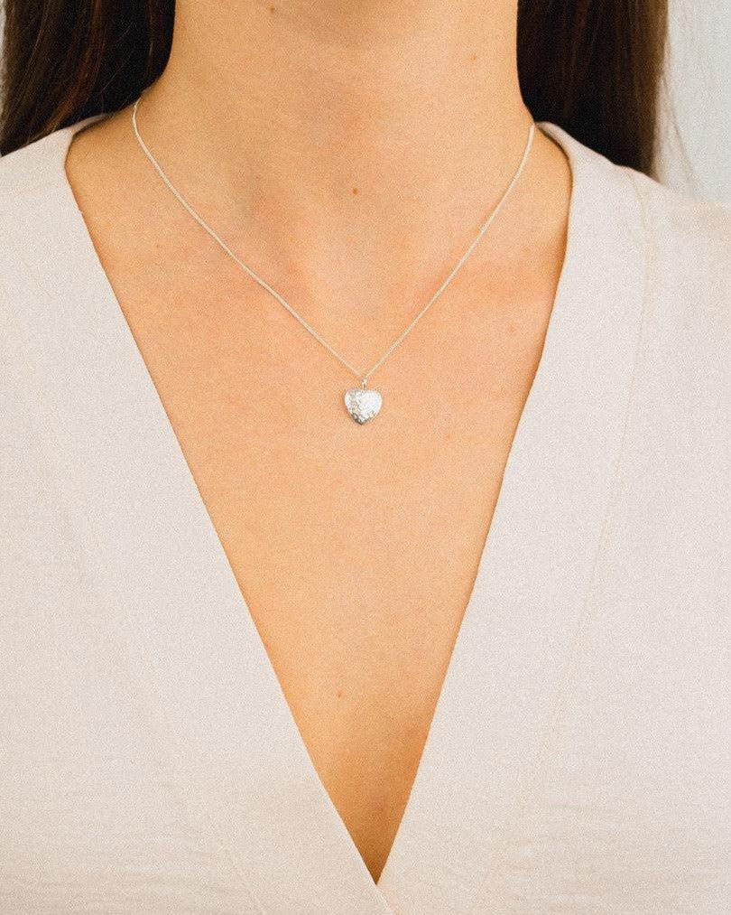Hammered silver heart pendant necklace on a woman wearing a V-neck top