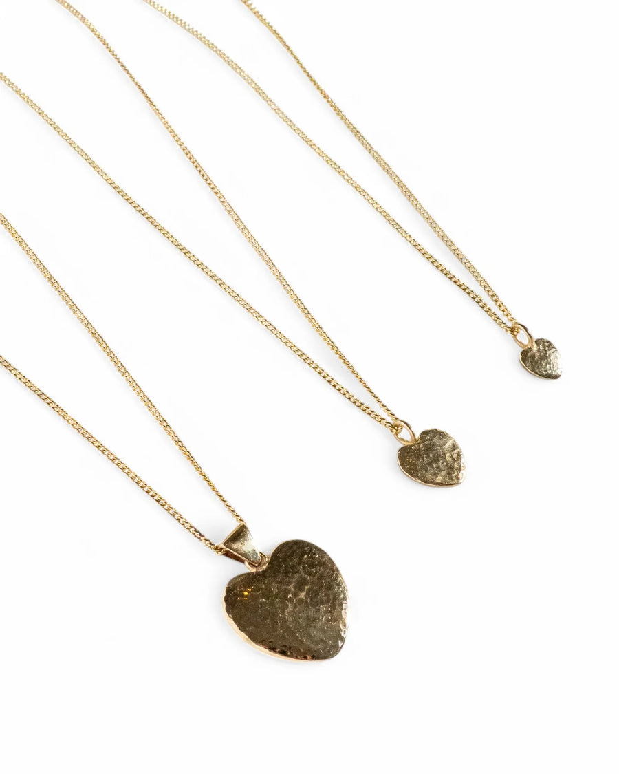 Three gold heart necklaces with hammered textured pendants on fine chains, white background