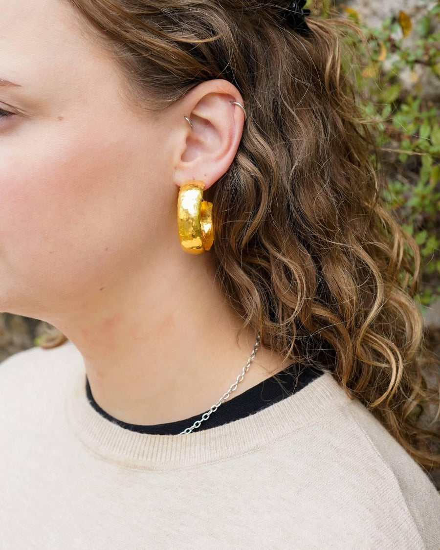 Woman wearing large hammered gold hoop earring and silver chain necklace outdoors