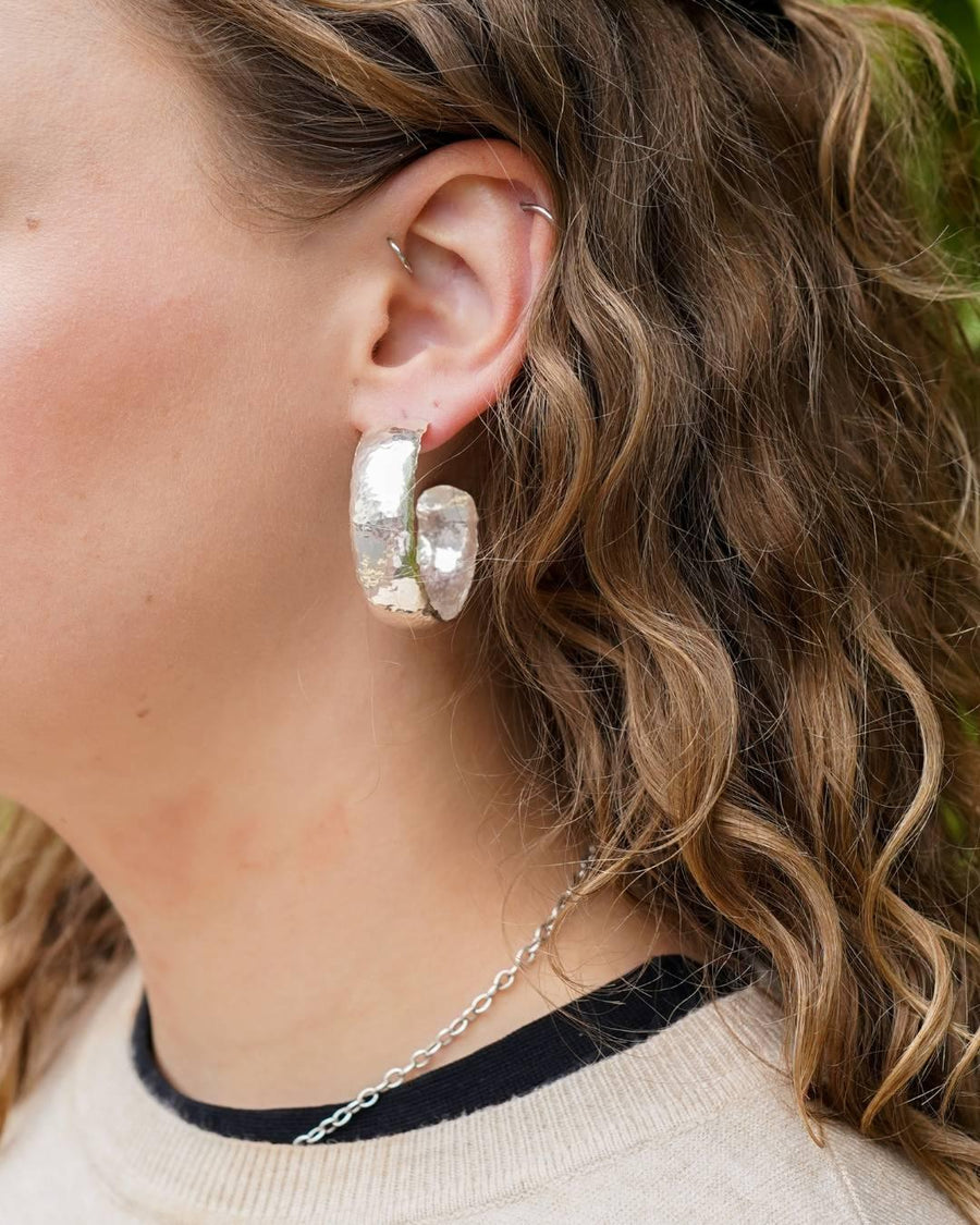 Woman wearing large handmade silver hoop earrings with organic texture and a delicate chain necklace