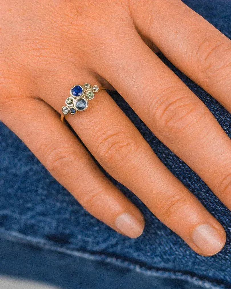 Cluster ring with sapphires and diamonds in platinum, worn on a hand with denim jeans