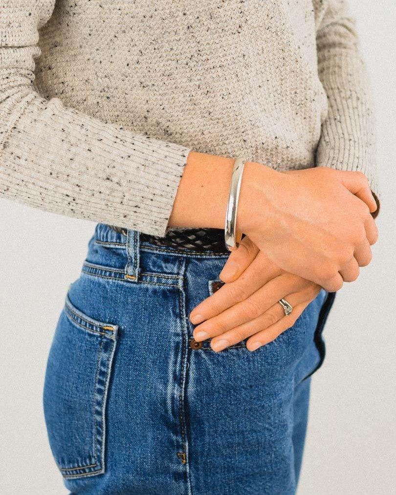 Solid silver hinged bangle on a wrist, worn with jeans and a sweater.