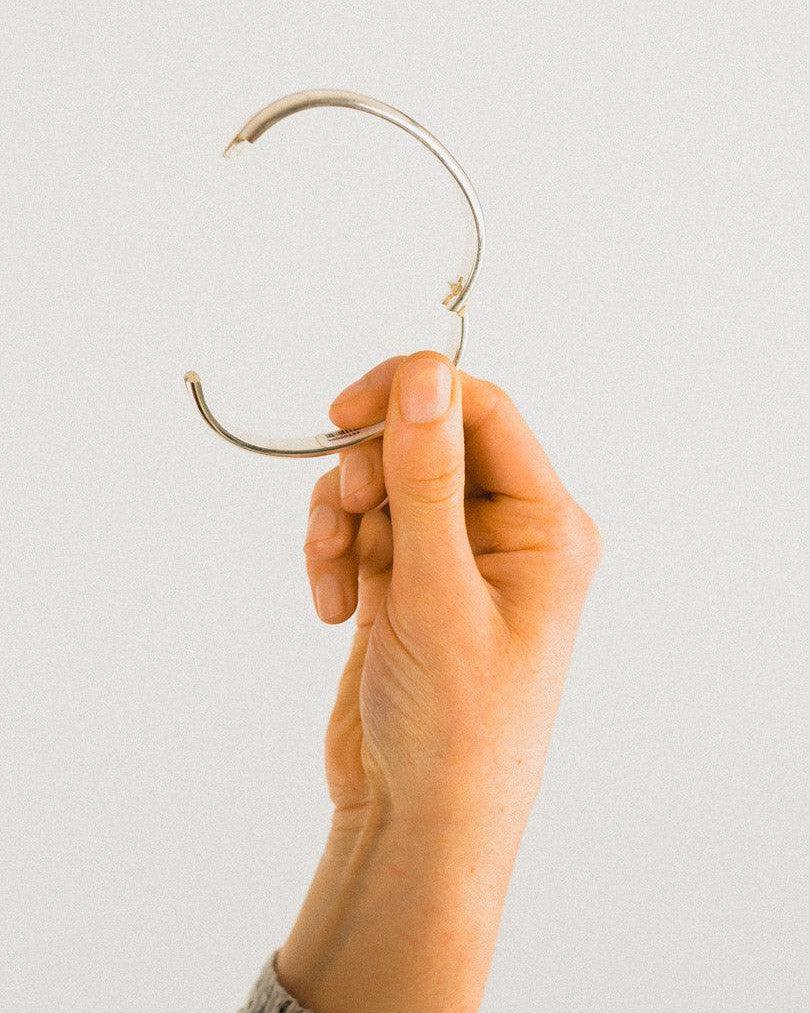 Hand holding a hinged solid silver diamond bangle.