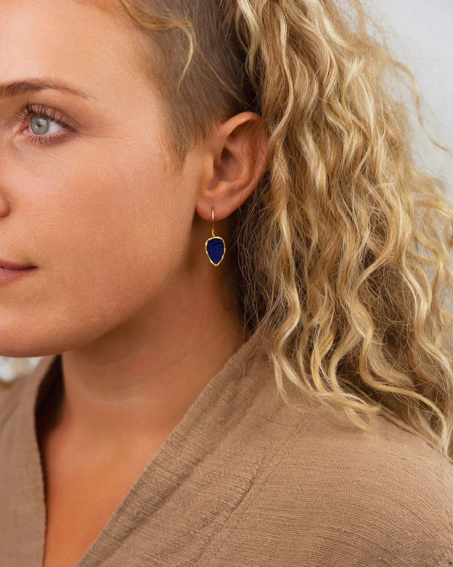 Woman wearing a gold drop earring with a deep blue lapis lazuli stone