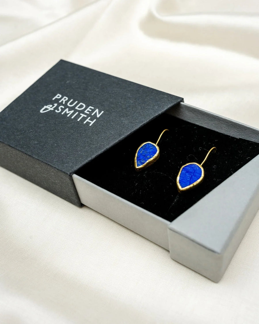 Gold lapis lazuli drop earrings with organic shape in a gift box on cream fabric