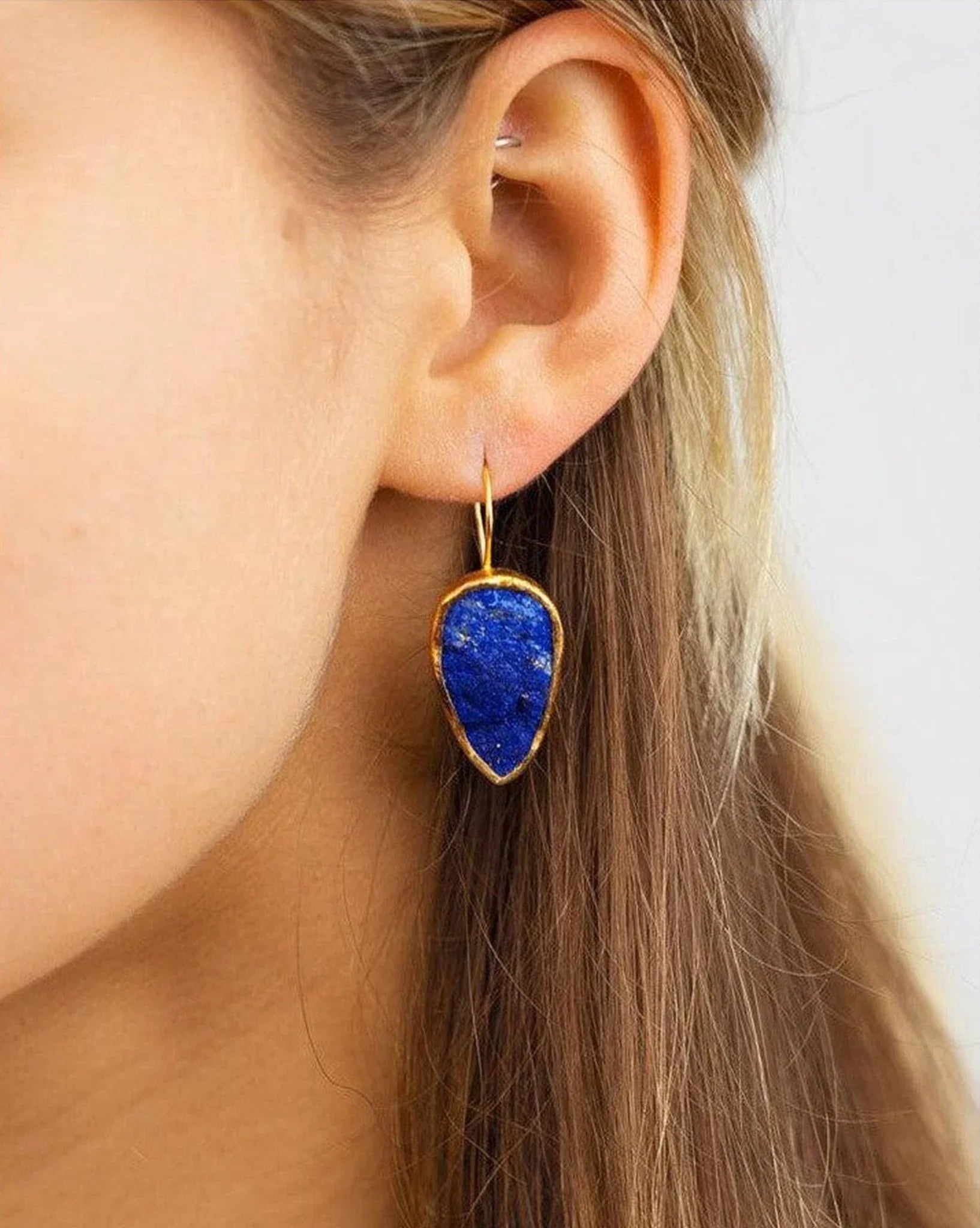 Handmade lapis lazuli drop earring with gold trim on a woman’s ear, luxury jewellery