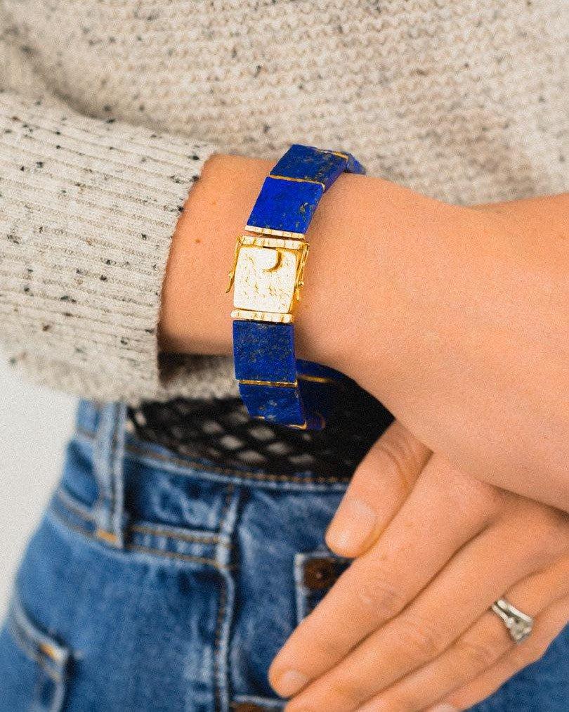 Hand wearing a gold lapis lazuli bracelet with bold blue stones, casual outfit visible