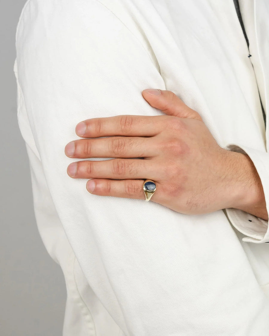 Lapis lazuli oval signet ring in yellow gold worn on a pinky finger.