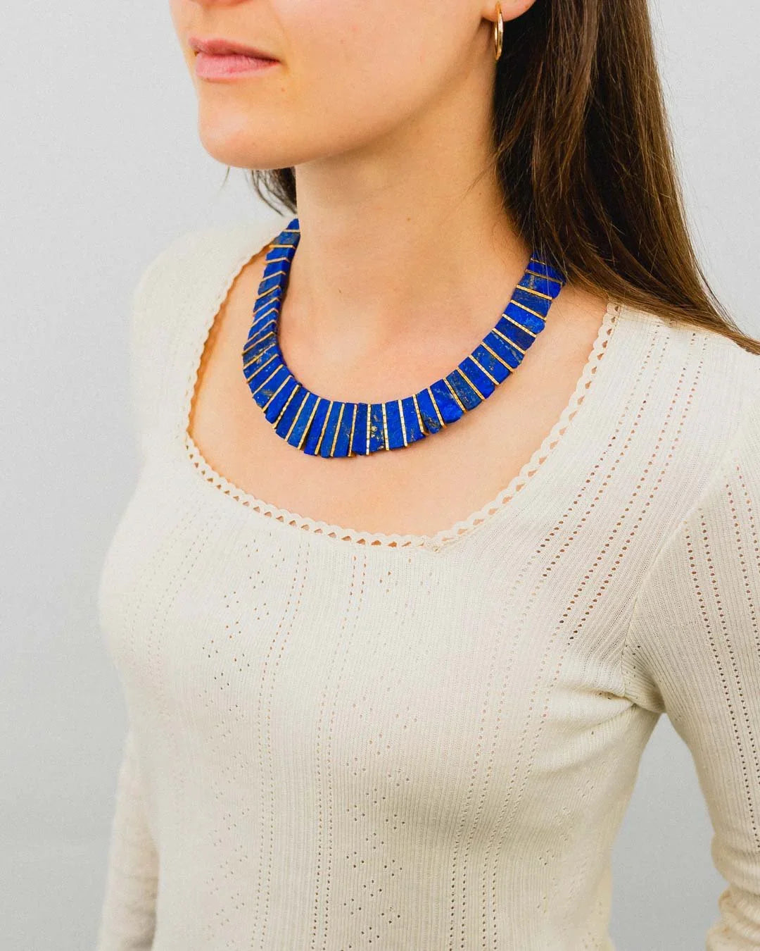 Woman wearing a blue lapis lazuli tab necklace with gold accents, styled on a cream knit top